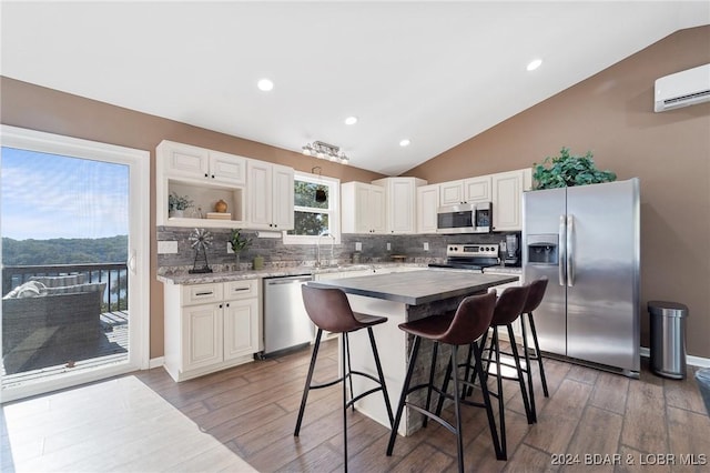 kitchen with hardwood / wood-style flooring, lofted ceiling, stainless steel appliances, and a wall mounted air conditioner