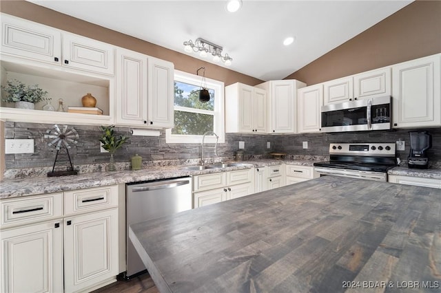 kitchen featuring lofted ceiling, butcher block counters, sink, appliances with stainless steel finishes, and backsplash