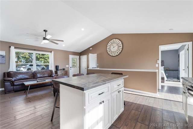 kitchen featuring a kitchen bar, white cabinetry, a center island, vaulted ceiling, and hardwood / wood-style floors