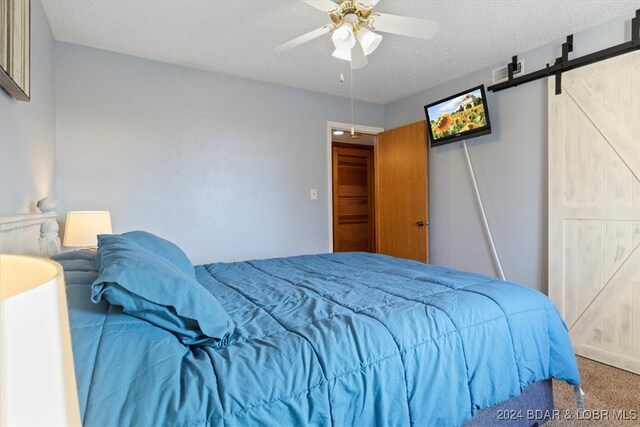 bedroom with carpet flooring, a textured ceiling, ceiling fan, and a barn door