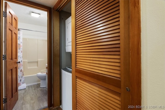 corridor with a textured ceiling, stacked washer and clothes dryer, and hardwood / wood-style flooring