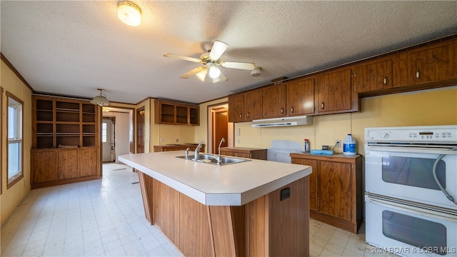 kitchen with ceiling fan, white double oven, sink, a textured ceiling, and a center island with sink