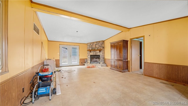 unfurnished living room with french doors, vaulted ceiling with beams, a stone fireplace, and wood walls