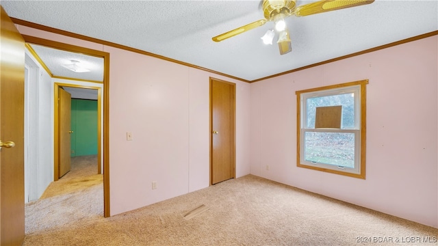 unfurnished bedroom with ceiling fan, light carpet, a textured ceiling, and ornamental molding