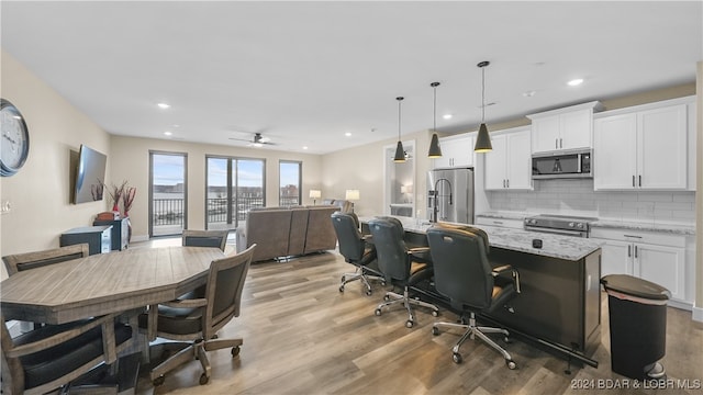 interior space with white cabinetry, hanging light fixtures, light stone counters, a kitchen island with sink, and appliances with stainless steel finishes