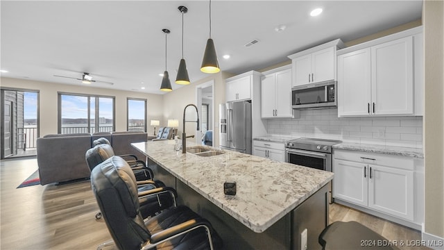 kitchen with appliances with stainless steel finishes, a center island with sink, hanging light fixtures, and ceiling fan