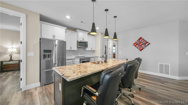 kitchen featuring a kitchen bar, appliances with stainless steel finishes, a kitchen island with sink, hardwood / wood-style flooring, and white cabinetry