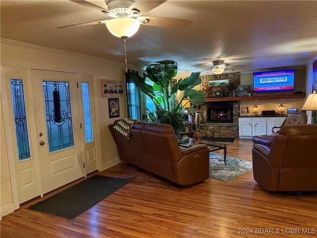 living room with hardwood / wood-style flooring, ceiling fan, ornamental molding, and a fireplace