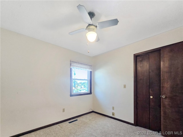 unfurnished bedroom featuring ceiling fan, light colored carpet, and a closet