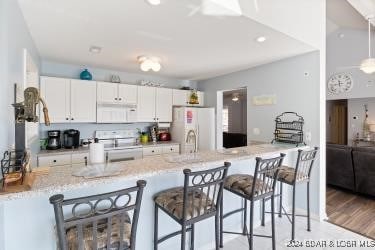 kitchen with kitchen peninsula, white cabinets, white appliances, and light wood-type flooring