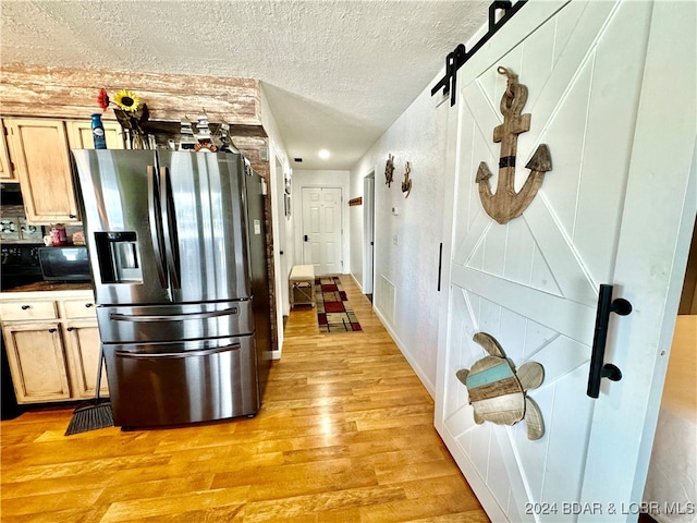 kitchen with stainless steel fridge, light wood-type flooring, a textured ceiling, light brown cabinets, and a barn door