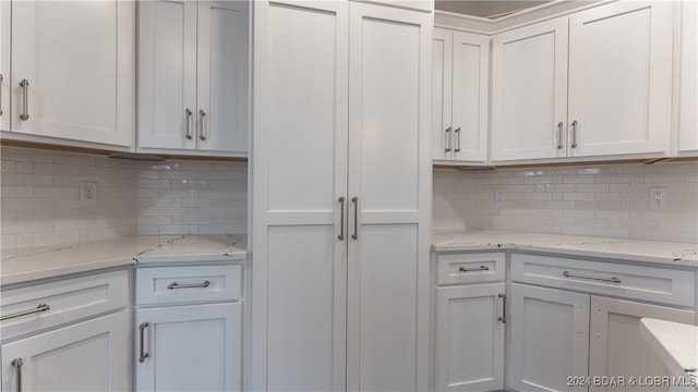 kitchen with light stone countertops, white cabinets, and backsplash