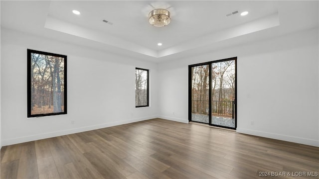 spare room featuring a raised ceiling, visible vents, baseboards, and wood finished floors