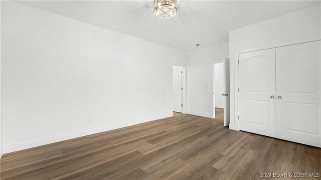 unfurnished bedroom featuring a closet, baseboards, and dark wood-type flooring