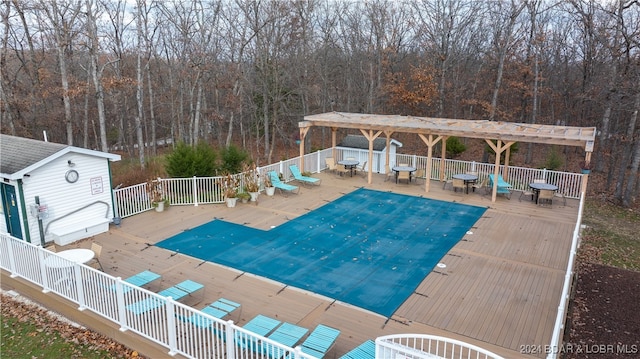 community pool with a wooded view, a wooden deck, and fence