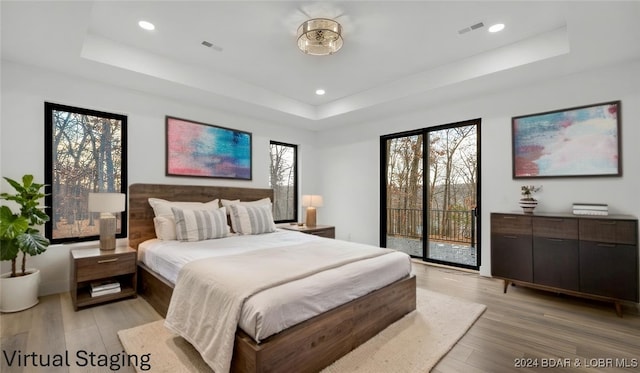 bedroom featuring a raised ceiling, light wood-style flooring, and access to exterior