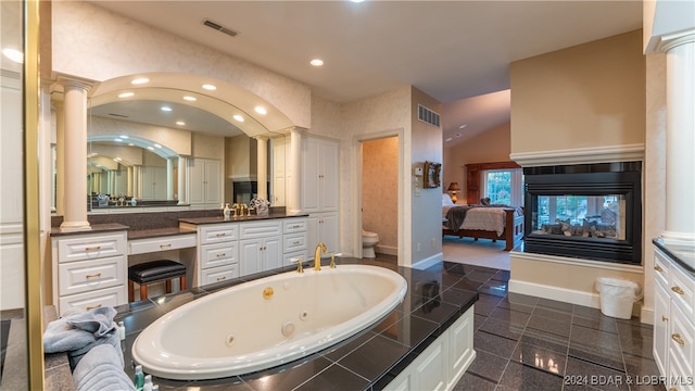 bathroom with vanity, a multi sided fireplace, toilet, ornate columns, and tiled tub