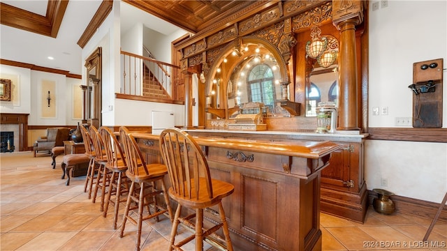 bar with a tile fireplace, light tile patterned floors, a towering ceiling, and ornamental molding