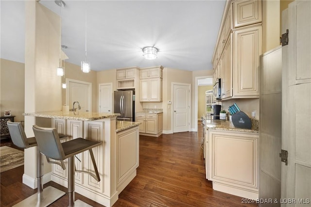 kitchen featuring pendant lighting, a breakfast bar, dark wood-type flooring, cream cabinets, and stainless steel appliances