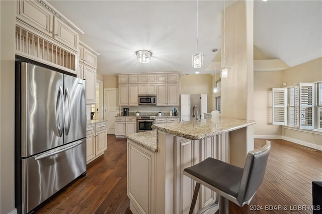 kitchen featuring light stone countertops, decorative light fixtures, cream cabinetry, a kitchen bar, and appliances with stainless steel finishes