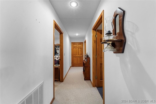 hallway featuring light colored carpet and a textured ceiling