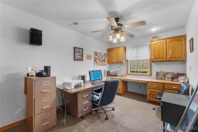 carpeted office featuring ceiling fan, built in desk, and a textured ceiling