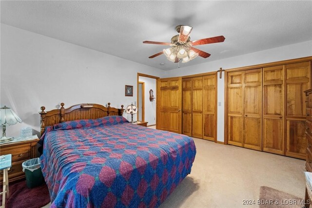 bedroom with light carpet, a textured ceiling, ceiling fan, and multiple closets