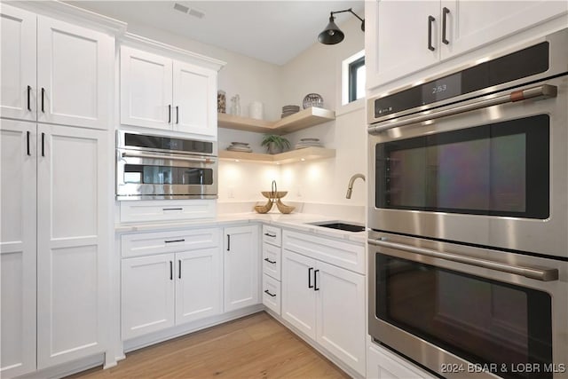 kitchen with light wood-type flooring, stainless steel appliances, white cabinetry, and sink