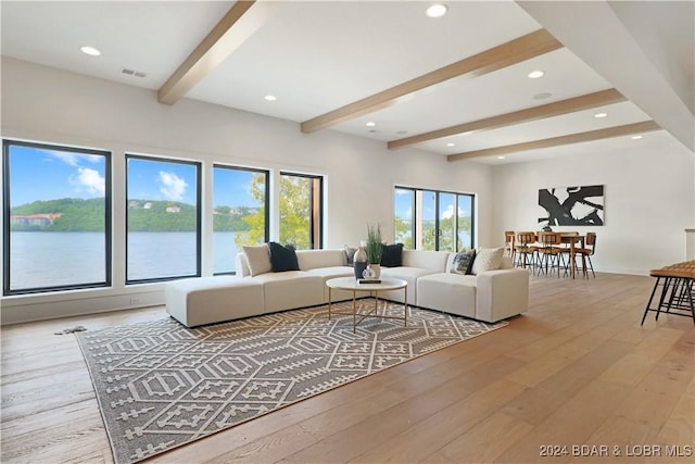 living room featuring beamed ceiling, light wood-type flooring, and a water view