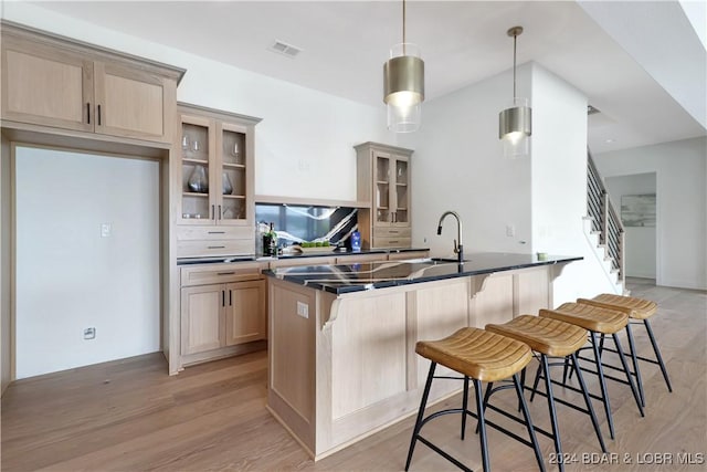 kitchen featuring an island with sink, light brown cabinetry, decorative light fixtures, light hardwood / wood-style floors, and a kitchen bar