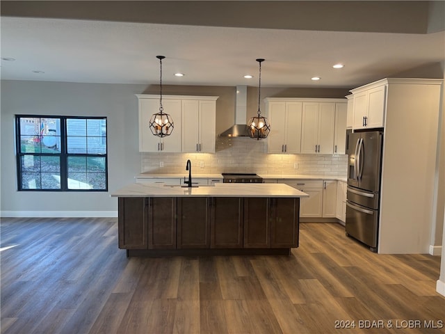 kitchen with pendant lighting, stainless steel appliances, a center island with sink, and wall chimney range hood