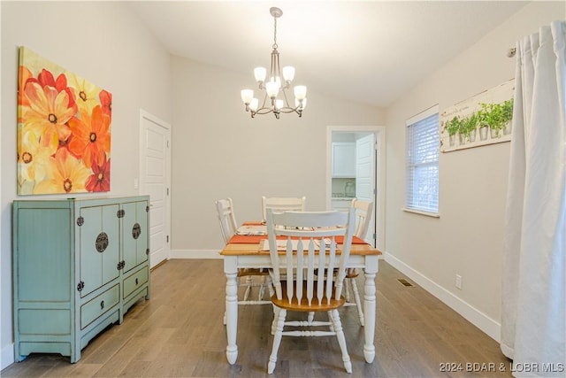 dining room featuring hardwood / wood-style floors, an inviting chandelier, and vaulted ceiling