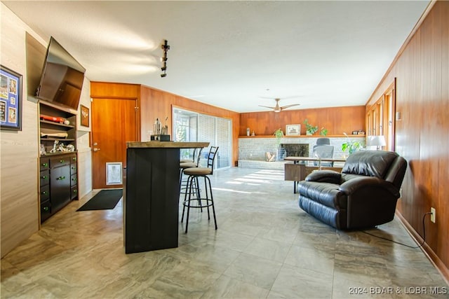 kitchen with ceiling fan, wooden walls, a kitchen breakfast bar, track lighting, and a brick fireplace