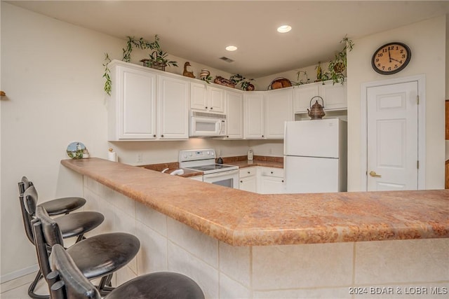 kitchen featuring white cabinets, white appliances, kitchen peninsula, and a breakfast bar area