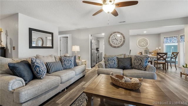 living room featuring visible vents, wood finished floors, a textured ceiling, and ceiling fan