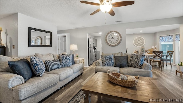 living room featuring hardwood / wood-style flooring, ceiling fan, and a textured ceiling