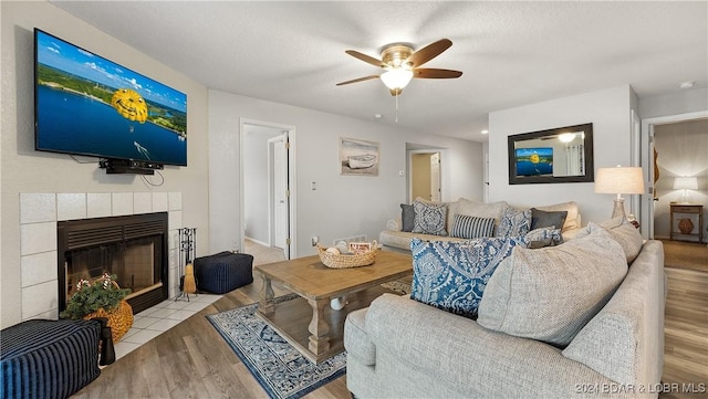 living room featuring ceiling fan, light hardwood / wood-style floors, a textured ceiling, and a tile fireplace