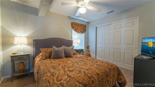 carpeted bedroom with ceiling fan, a closet, and beamed ceiling