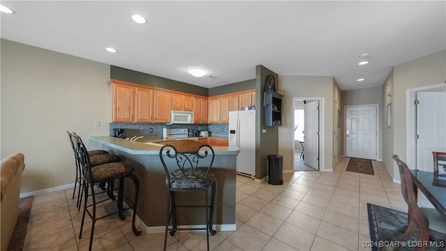 kitchen featuring kitchen peninsula, a kitchen breakfast bar, backsplash, white appliances, and light tile patterned floors