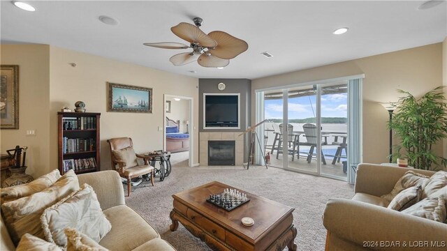 carpeted living room with ceiling fan and a tiled fireplace