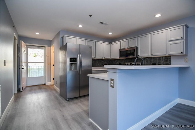 kitchen with backsplash, kitchen peninsula, light hardwood / wood-style flooring, and appliances with stainless steel finishes