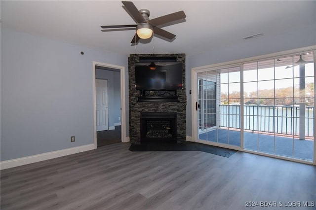 unfurnished living room featuring hardwood / wood-style flooring, ceiling fan, and a stone fireplace