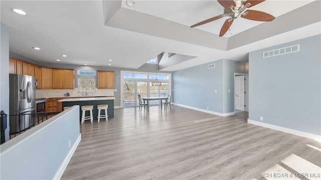 kitchen with a kitchen breakfast bar, ceiling fan, light wood-type flooring, tasteful backsplash, and stainless steel appliances