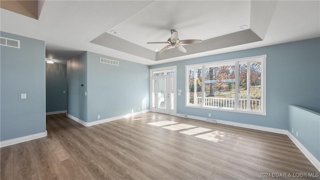 empty room featuring a raised ceiling, ceiling fan, and wood-type flooring