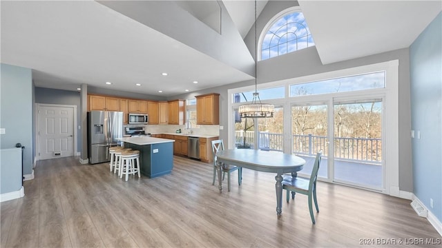 kitchen with a kitchen breakfast bar, stainless steel appliances, decorative light fixtures, light hardwood / wood-style floors, and a kitchen island