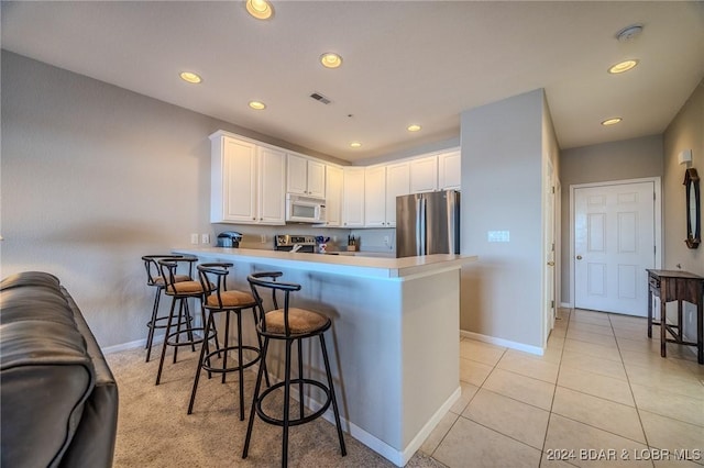 kitchen featuring appliances with stainless steel finishes, white cabinetry, a breakfast bar area, light tile patterned floors, and kitchen peninsula