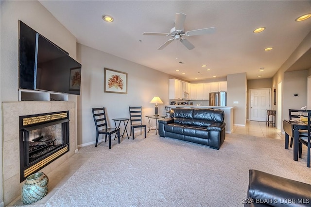 living room featuring ceiling fan, a tile fireplace, and light carpet