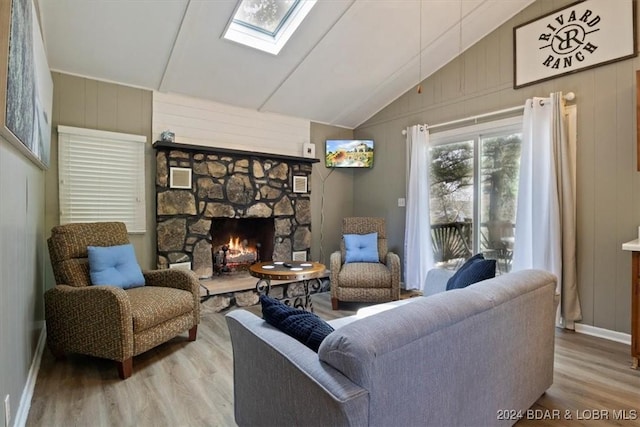 living room featuring light wood-type flooring, lofted ceiling with skylight, and a stone fireplace