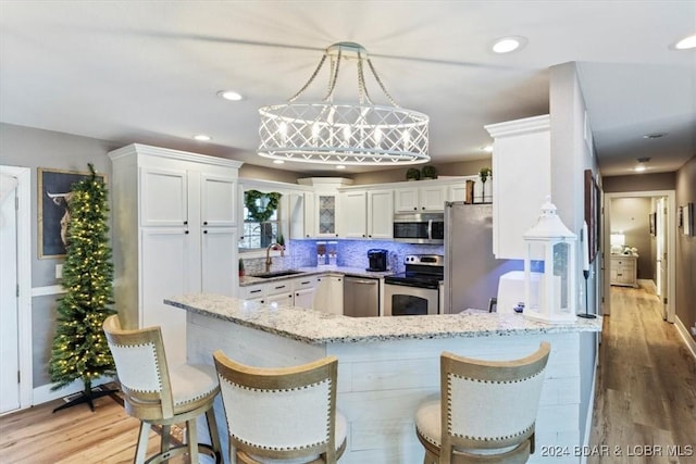 kitchen with white cabinetry, sink, decorative light fixtures, appliances with stainless steel finishes, and light wood-type flooring