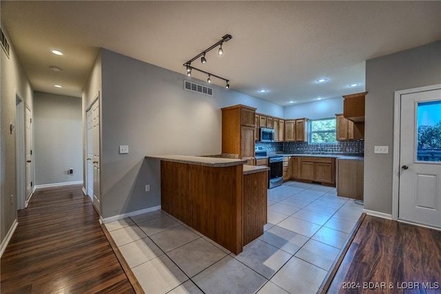 kitchen with sink, decorative backsplash, light hardwood / wood-style floors, kitchen peninsula, and stainless steel appliances